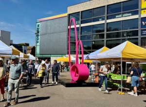 Yellow and white market stalls and a bright pink sculpture in front of the Towner gallery, creating a colourful scene full of people
