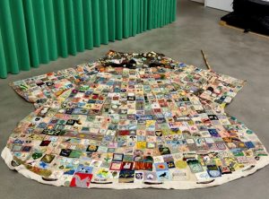 a large patchwork coat laid on ground. the coat is made of many different embroidered sqaures