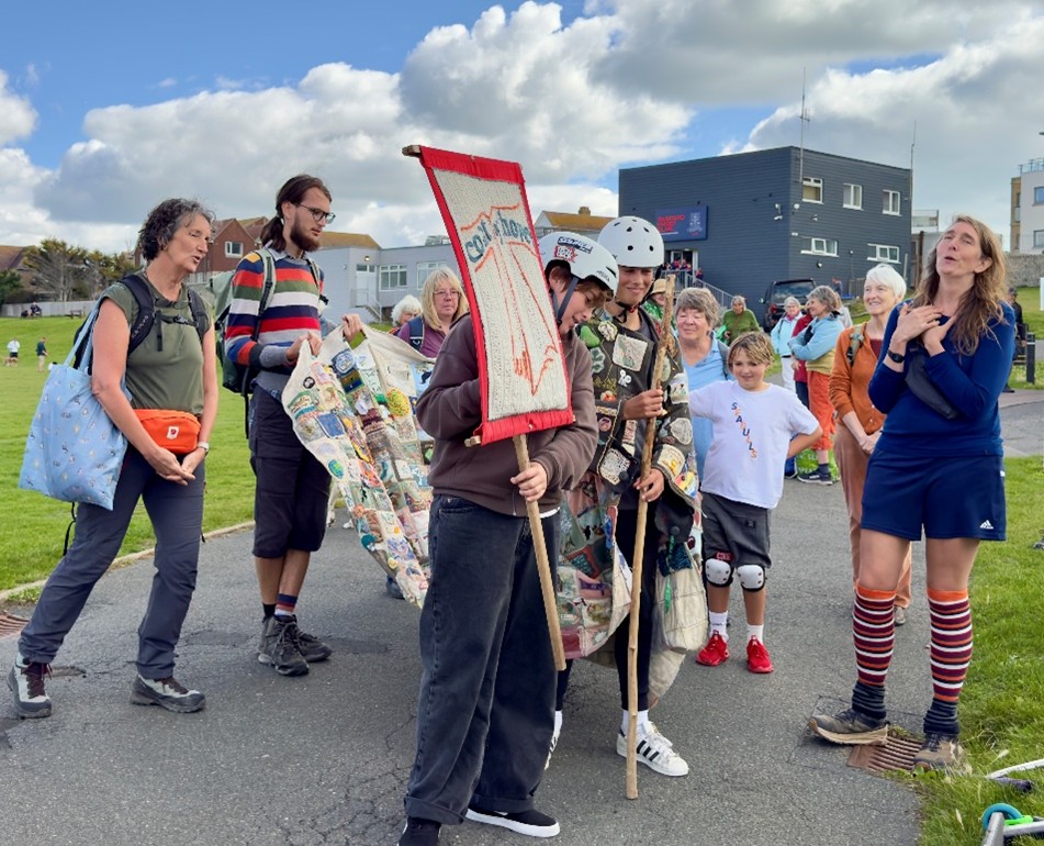 group of people on footpath looking at the coat of hopes. one person is singing