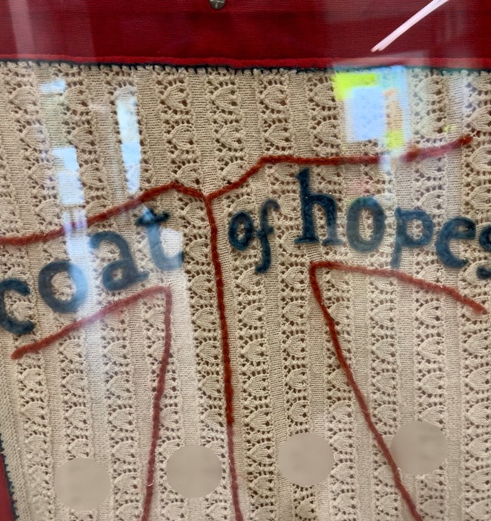 Embroidered symbol of the Coat of Hopes on a lacey knitted background