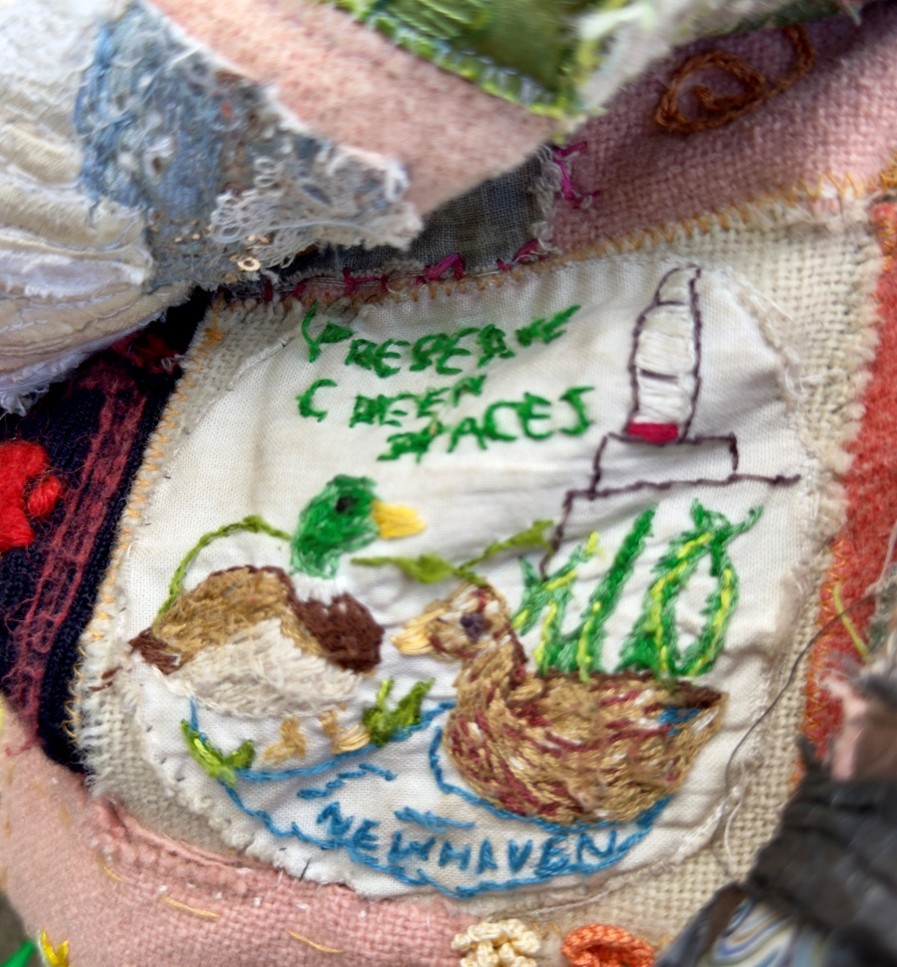 Part of a patchwork quilt showing small patch with two embroidered ducks and the words 'Preserve green spaces' above and 'Newhaven' underneath